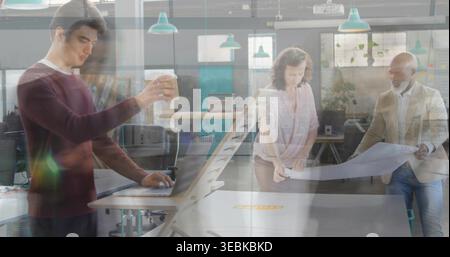 Working three colleagues unfolding blueprint and checking laptop in studio, wearing maroon sweater Stock Photo
