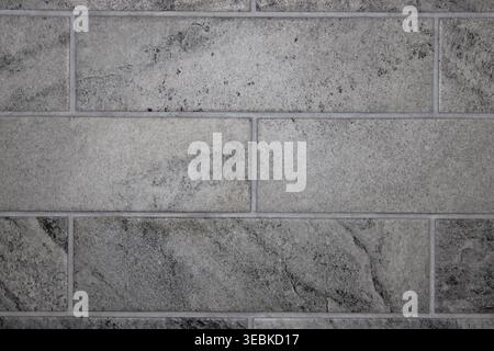 A wall covered with gray rectangular tiles forms a solid surface in a contemporary area. No decorations are present on the wall, giving it a clean loo Stock Photo
