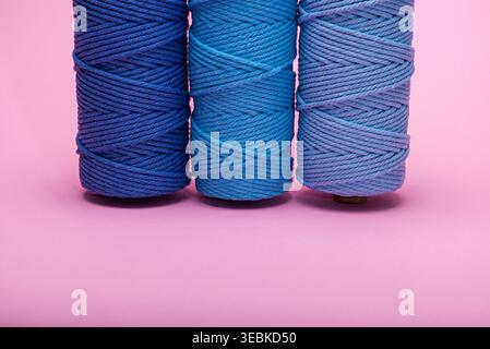 Three spools of woven cord in different shades of blue, displayed on a bright pink backdrop. Stock Photo