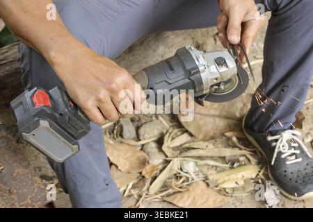 Focused worker holding cordless angle grinder tool with wrench adjusting cutting disc outdoors on ground covered with dry leaf preparing equipment for Stock Photo