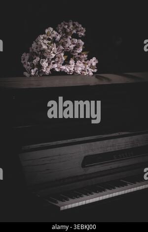Vintage upright piano with decorative blossom branches in a dark atmospheric interior Stock Photo