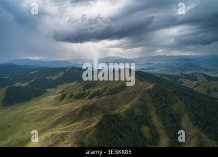Altai Mountains landscape view with dark storm clouds and sun rays breaking through, illuminating green forest and valleys Stock Photo