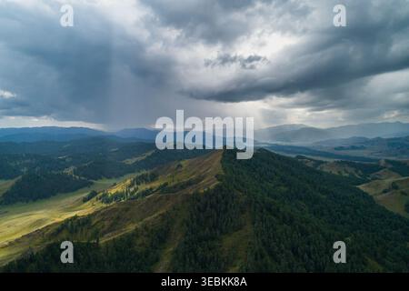Altai Mountains landscape view with dark storm clouds and sun rays breaking through, illuminating green forest and valleys Stock Photo