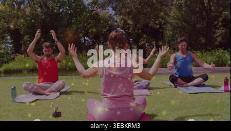 Leading instructor guiding group on yoga mats on park lawn wearing tank tops, with water bottles Stock Photo