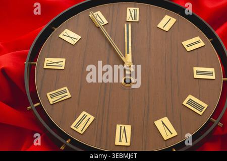 Vintage wall clock with wooden dial on red fabric showing five minutes to twelve Stock Photo