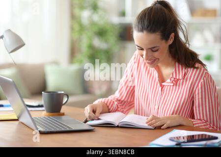 Happy woman working at home checking paper agenda on a wooden table Stock Photo