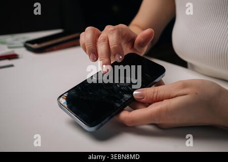 Woman peeling damaged screen protector from smartphone, exposing cracked protective film on white surface, revealing device compromised condition. Stock Photo