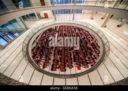 Dhaka, Bangladesh - 19 March 2025: View of a large corporate event in a circular atrium, vibrant red tables packed with dark-suited attendees under mo Stock Photo