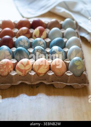 Carton with Colorful Naturally Dyed Easter Eggs on Table Stock Photo
