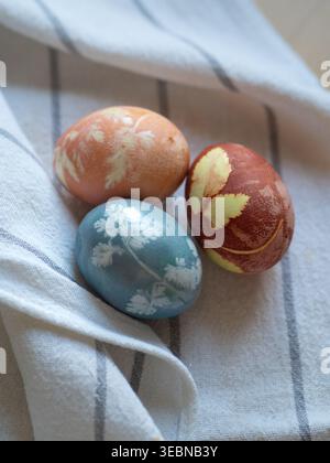 Three Naturally Dyed Eggs With Floral Imprints on White Linen Stock Photo