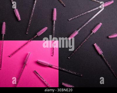 A mix of clear and pink brow brushes are scattered across a dark background with a bright pink area The scene highlights tools used for beauty and mak Stock Photo
