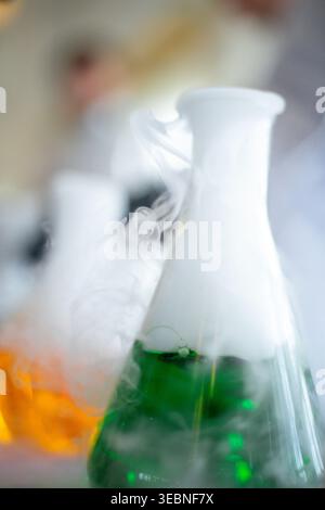 People conduct a chemistry fun experiment with colorful liquids in glass flasks as smoke rises. The setting is a science lab, and reactions create int Stock Photo