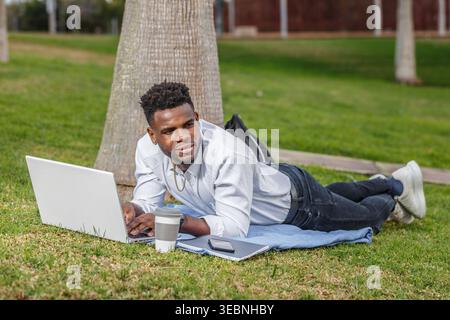 An African-American man working on his laptop while on the park floor. Stock Photo