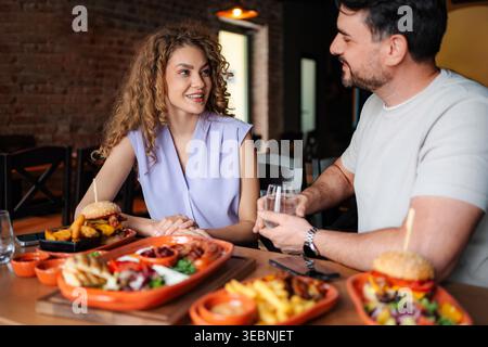 Young couple having lunch together at a restaurant, eating burgers and drinking water Stock Photo
