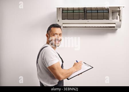 Worker inspecting an indoor air conditioning unit and writing on a clipboard Stock Photo