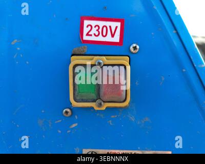 Electrical control buttons with 230v label on blue machine panel close up with dust and wear marks. Industrial equipment control, electricity, safety. Stock Photo