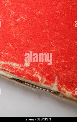 Detailed macro view showcasing the rough texture of red handmade paper with embedded fibers and a silver staple holding layers together Stock Photo