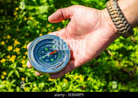 Hand holding magnetic compass in green mountain forest outdoor, hiking navigation adventure travel Stock Photo