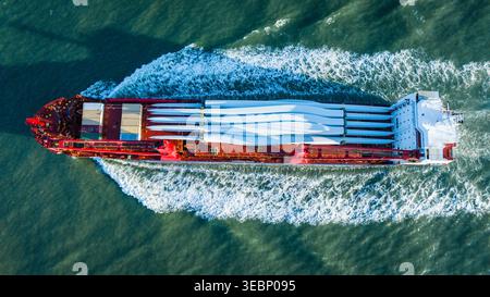 Aerial view of a vast cargo ship cutting through the water, carrying wind turbine blades creating a striking contrast against the deep blue sea, Freep Stock Photo