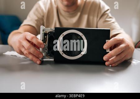 Close-up view of technician working with electronic device, holding computer hardware with exposed cooling fan, performing repairs and maintenance on Stock Photo