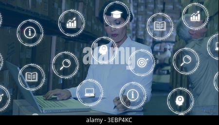 Working woman white-shirt checking laptop on box, writing on clipboard in warehouse aisle with HUD Stock Photo