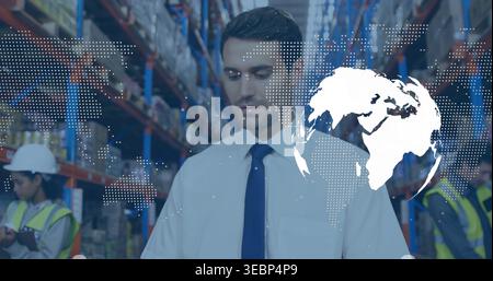 Standing manager in white shirt and dark tie scanning racks, workers with tablet, globe overlay Stock Photo
