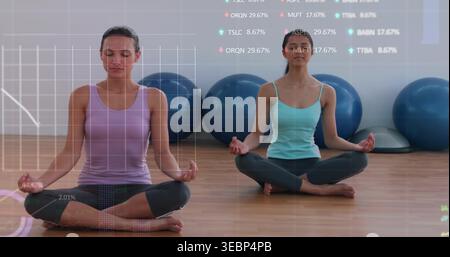 Sitting two women meditating in yoga studio, with blue balls, BOSU and charts, wearing tanks Stock Photo