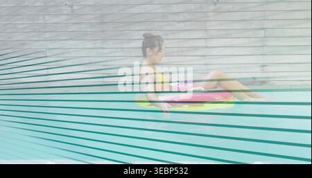 Floating woman wearing yellow bikini in pool near wooden slats, with pink inflatable ring Stock Photo
