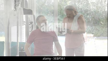 Exercising couple wearing maroon tee and pale pink top using bench, holding tablet in home gym Stock Photo