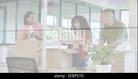 Inspecting woman wearing rust cardigan, examining framed item at desk in office with boxes and tape Stock Photo