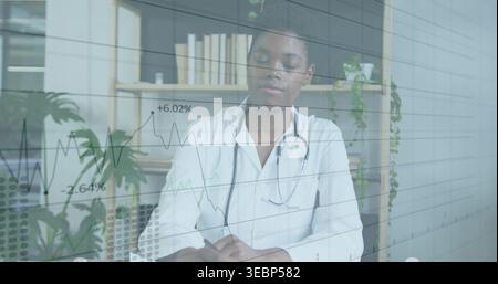 Writing doctor in white coat with stethoscope taking notes at clinic with pen, glass chart overlay Stock Photo