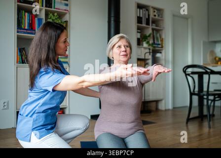 Physiotherapist helping senior woman during rehabilitation exercise at home. Stock Photo