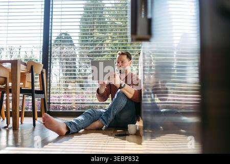 Man using smart home app working on tablet and sitting on floor. Stock Photo