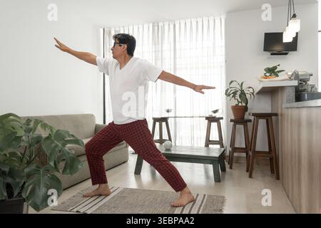 Middle aged man practicing yoga warrior pose at home Stock Photo