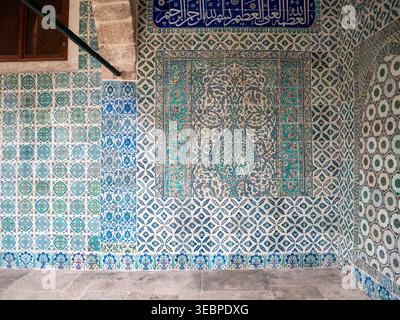 Beautiful wall covered in ornate traditional Islamic ceramic tiles featuring intricate geometric floral patterns in blue and white with calligraphy Stock Photo