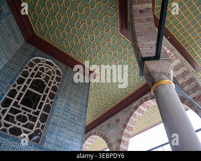 Ancient Ottoman architecture featuring intricate green and gold geometric ceiling tiles with blue Iznik ceramic walls and stone columns in Istanbul Stock Photo