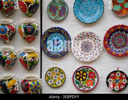 Colorful hand painted Turkish ceramic plates and vases featuring traditional Ottoman floral motifs and vibrant patterns on a white wall in Istanbul Stock Photo