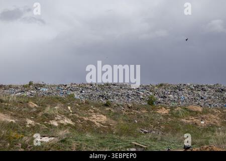 A large landfill is visible with various types of garbage piled up. The sky is grey with clouds above the site, indicating a possible rain in the area Stock Photo