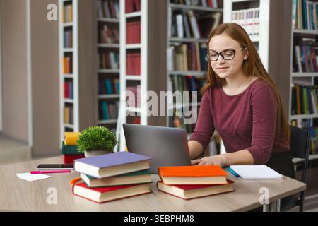 Young Woman Studying With Laptop and Books in a Modern Library Environment Stock Photo