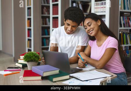 Young Students Collaborating on a Laptop in a Library Surrounded by Books Stock Photo