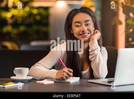 Young Woman Studying and Taking Notes in a Cozy Cafe During Daytime Stock Photo