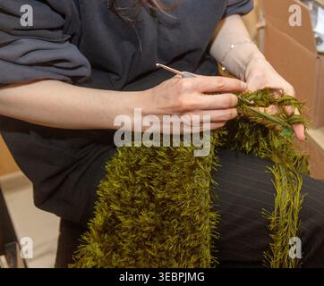 A person crocheting a textured woman handbag using a green, fringed yarn Stock Photo
