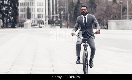 Man Rides Bicycle in Urban Area Wearing Suit and Glasses Near Modern Buildings in Bright Daylight Stock Photo