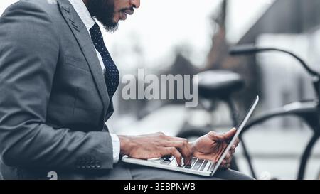 Man Works on Laptop While Sitting Outdoors Near Bicycle in Urban Area During Daytime Stock Photo