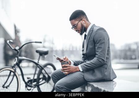 Professional Man Enjoying Coffee While Using Smartphone Near Bicycle in Urban Setting Stock Photo