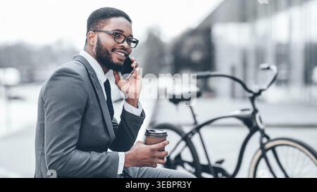 Businessman Talks on Phone While Sitting Near Bicycle in City Setting Stock Photo