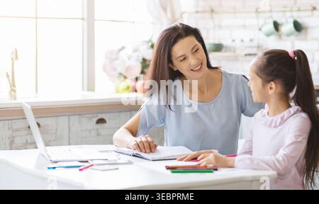Mother Helping Daughter With Homework in a Bright Kitchen During the Day Stock Photo