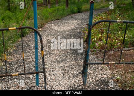 Gravel path leading through old metal gates into a wooded park Stock Photo