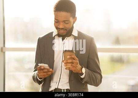 Young Man Enjoys Coffee While Texting at a Bright Modern Location in the City Stock Photo