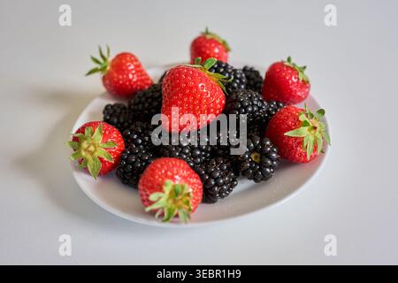 Fresh ripe strawberries and blackberries on a white plate over a white background. Healthy mixed berries for summer nutrition and antioxidant themes. Stock Photo